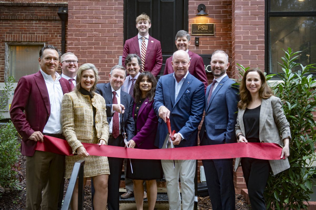 People pose and smile in front of a ribbon, holding scissors to the ribbon