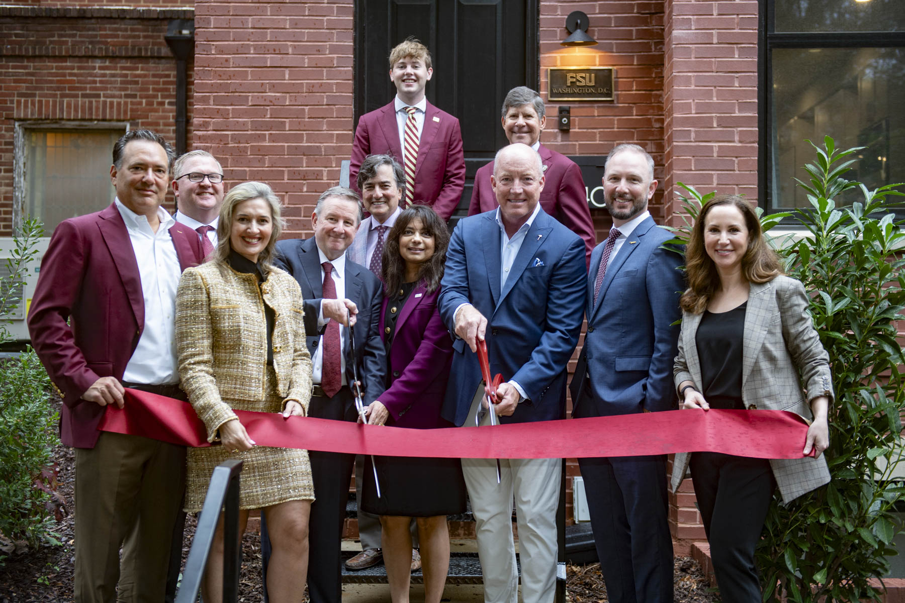 People pose and smile in front of a ribbon, holding scissors to the ribbon