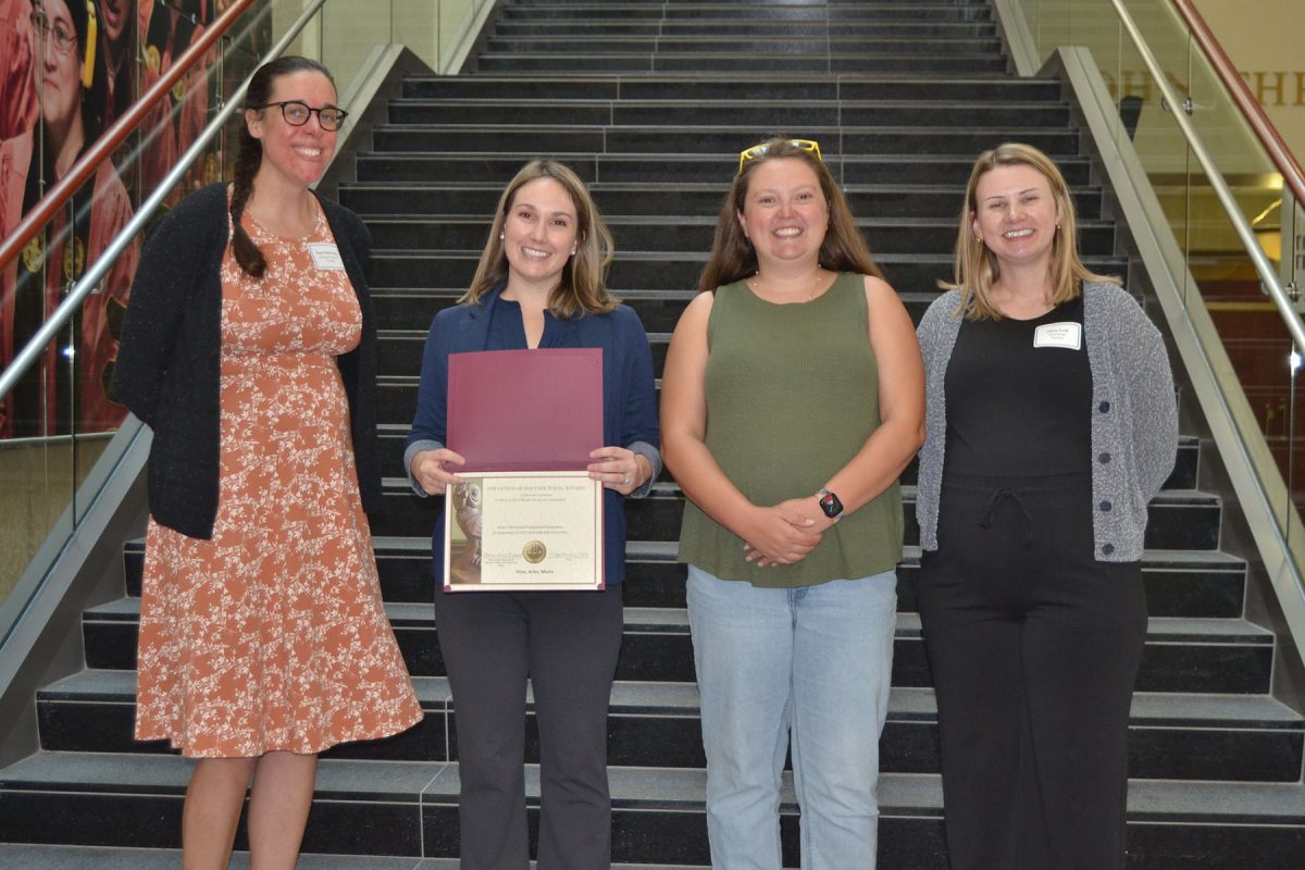 Four people smile and pose for a photo, one of them holding a piece of paper looking to be a certificate of some kind