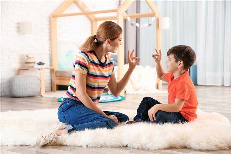 A woman and a child holding up hand signs, sitting on the floor