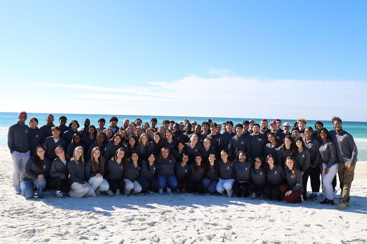 Many people wearing similar clothing posing for a photo on a beach