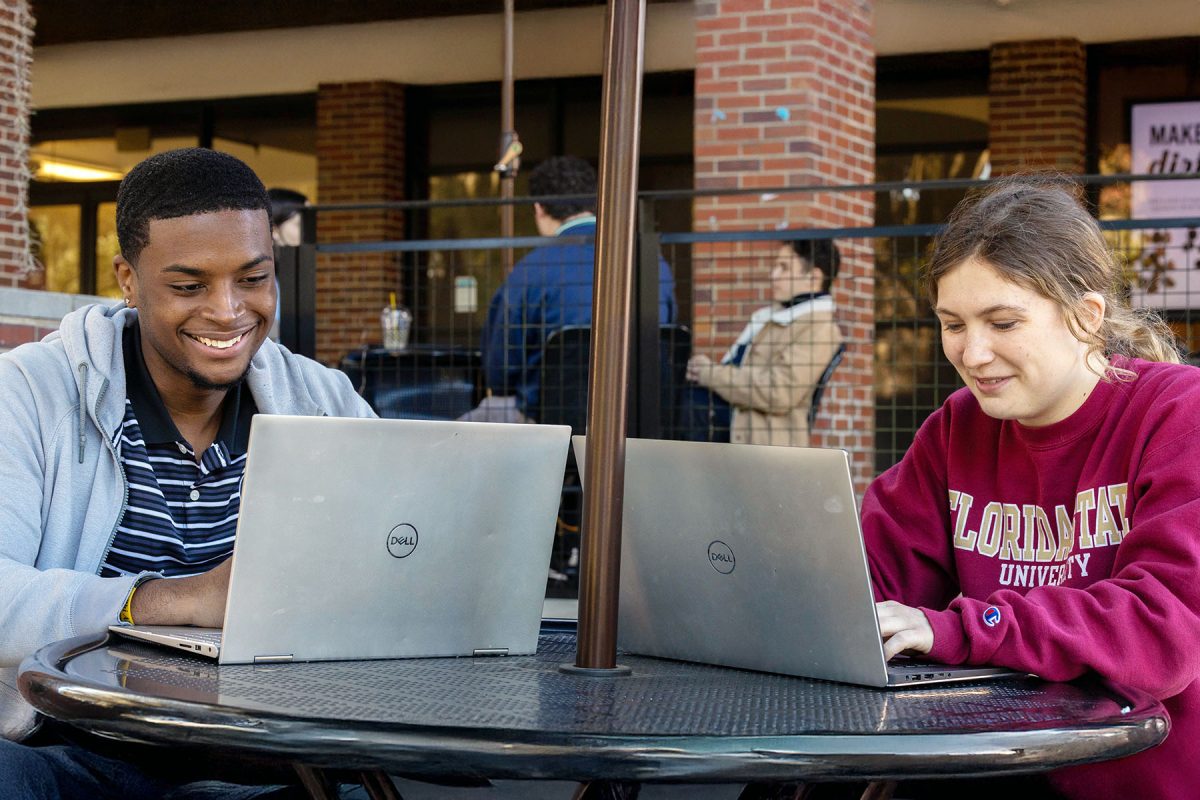 Two students smile, looking at their computers
