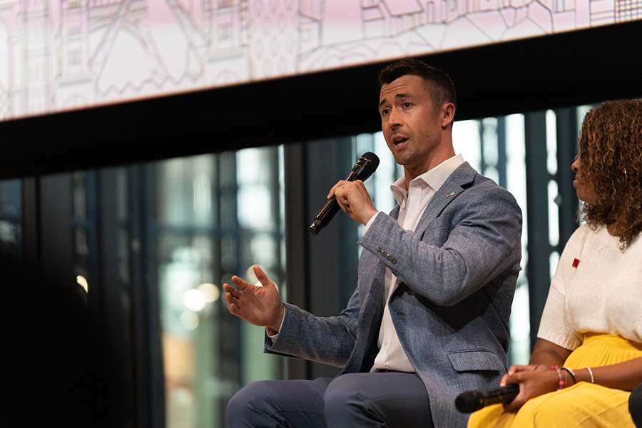 A man sits and speaks into a microphone, talking with his hands