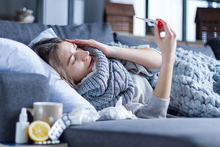 Sick woman on a couch looking at a thermometer