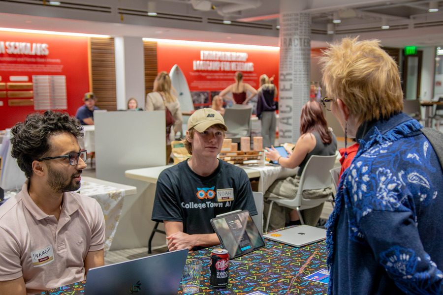 Women with her back to the camera speaking to two young men at a table