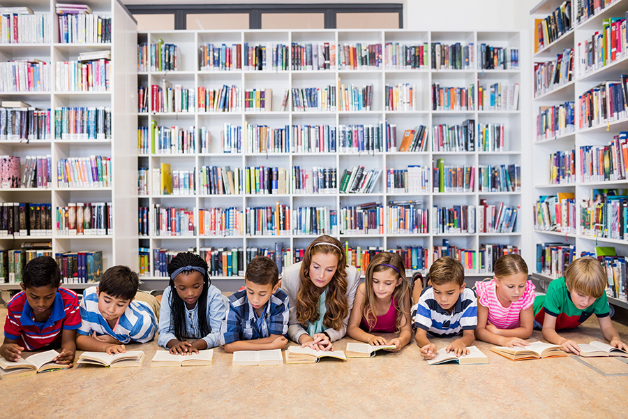 Children and their teacher lying down with books in a library
